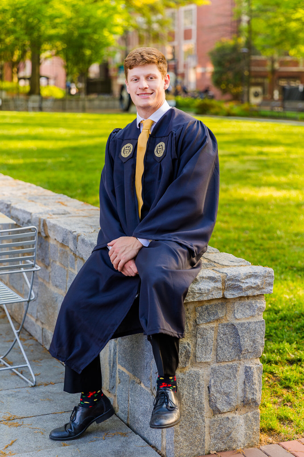 Georgia Tech University boy sitting on a campus wall wearing graduation gown outside during senior portraits with Atlanta photographer Laure Photography