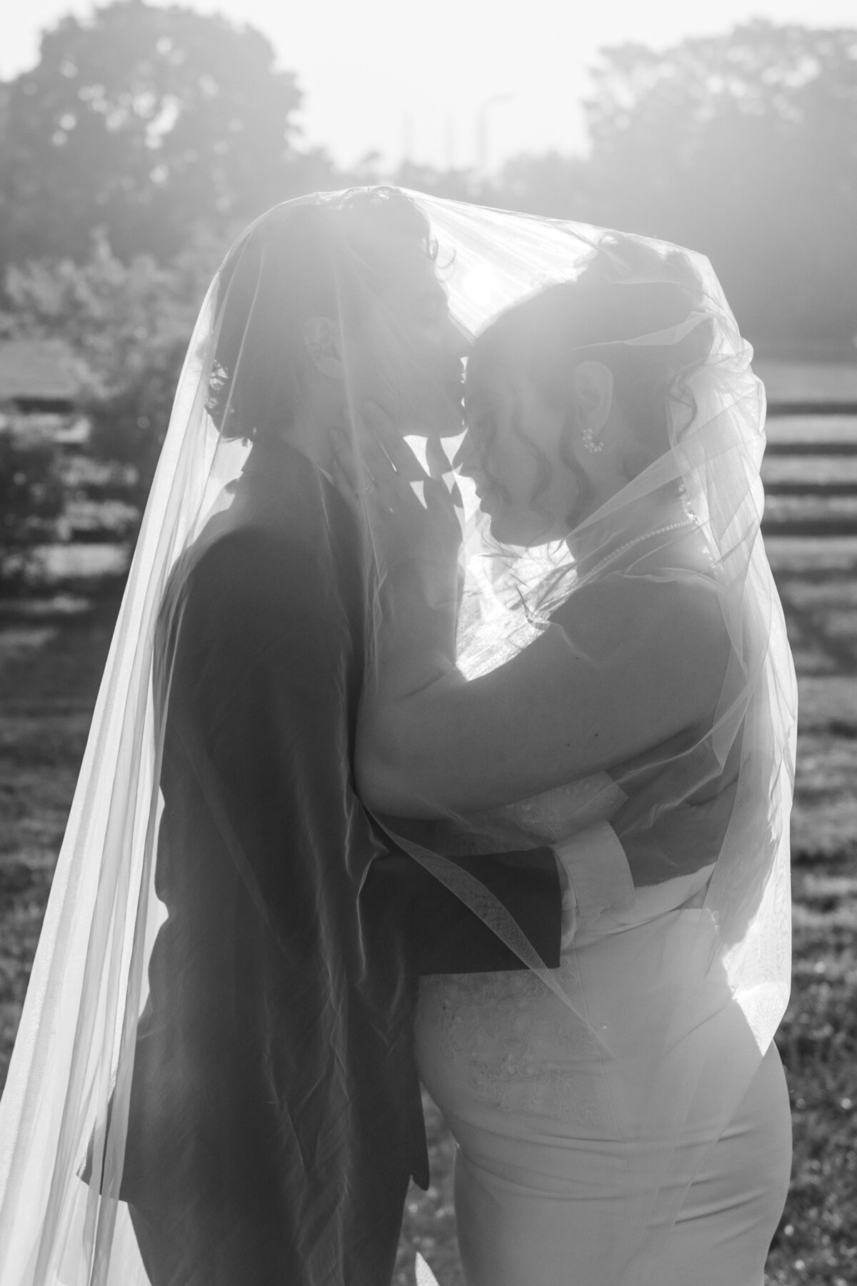 bride and groom under veil with sun shinning though