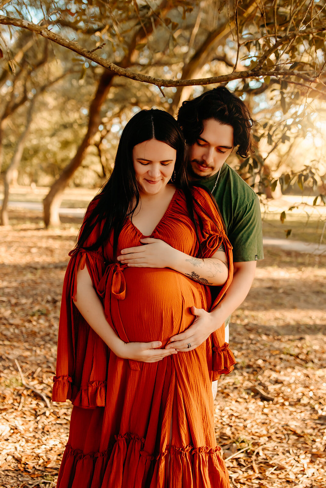 Houston maternity photographer – expecting couple embracing under oak trees, mother in burnt orange gown