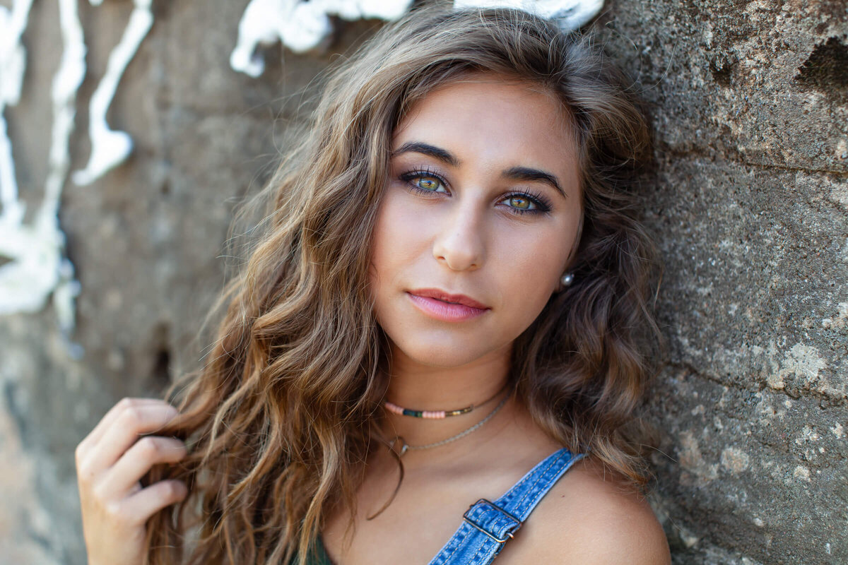 A beautiful green eyed teen leans against a concrete wall in this close up portrait. Captured by Springfield MO photographer Dynae Levingston.