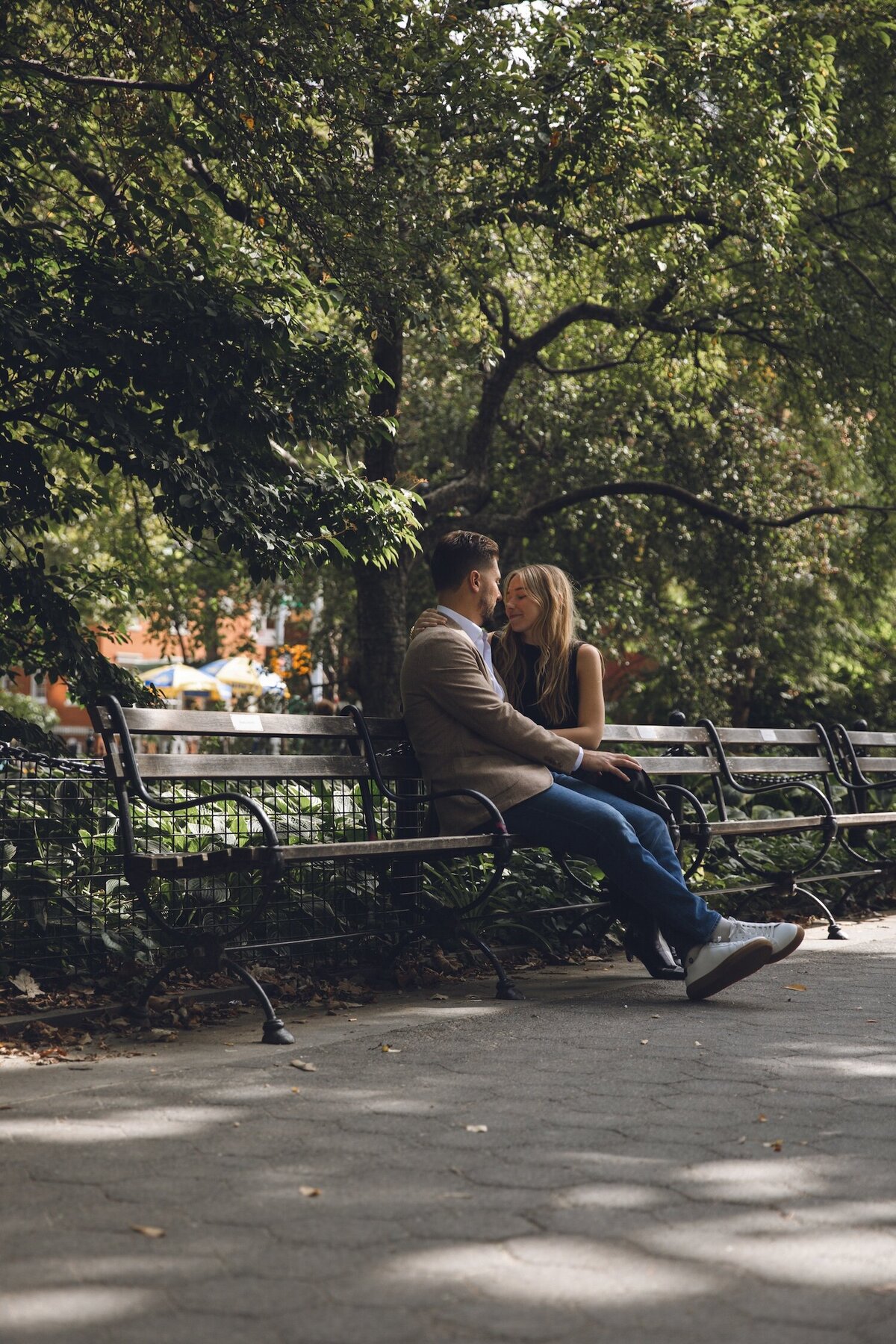 Tender moment between couple on a park bench under trees.