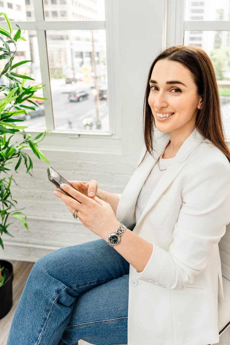 business coach sitting by window holding a phone in baltimore studio taken  by personal branding photographer