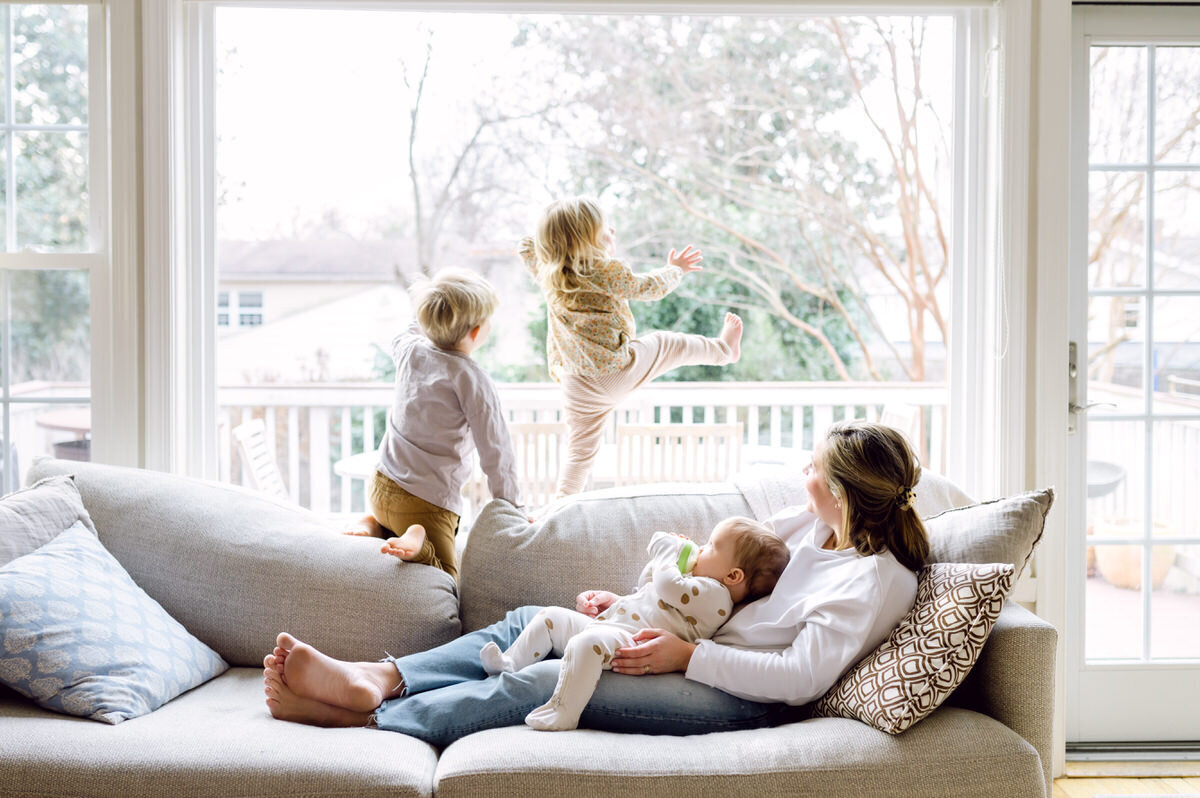 mom holding baby with kids playing on back of couch