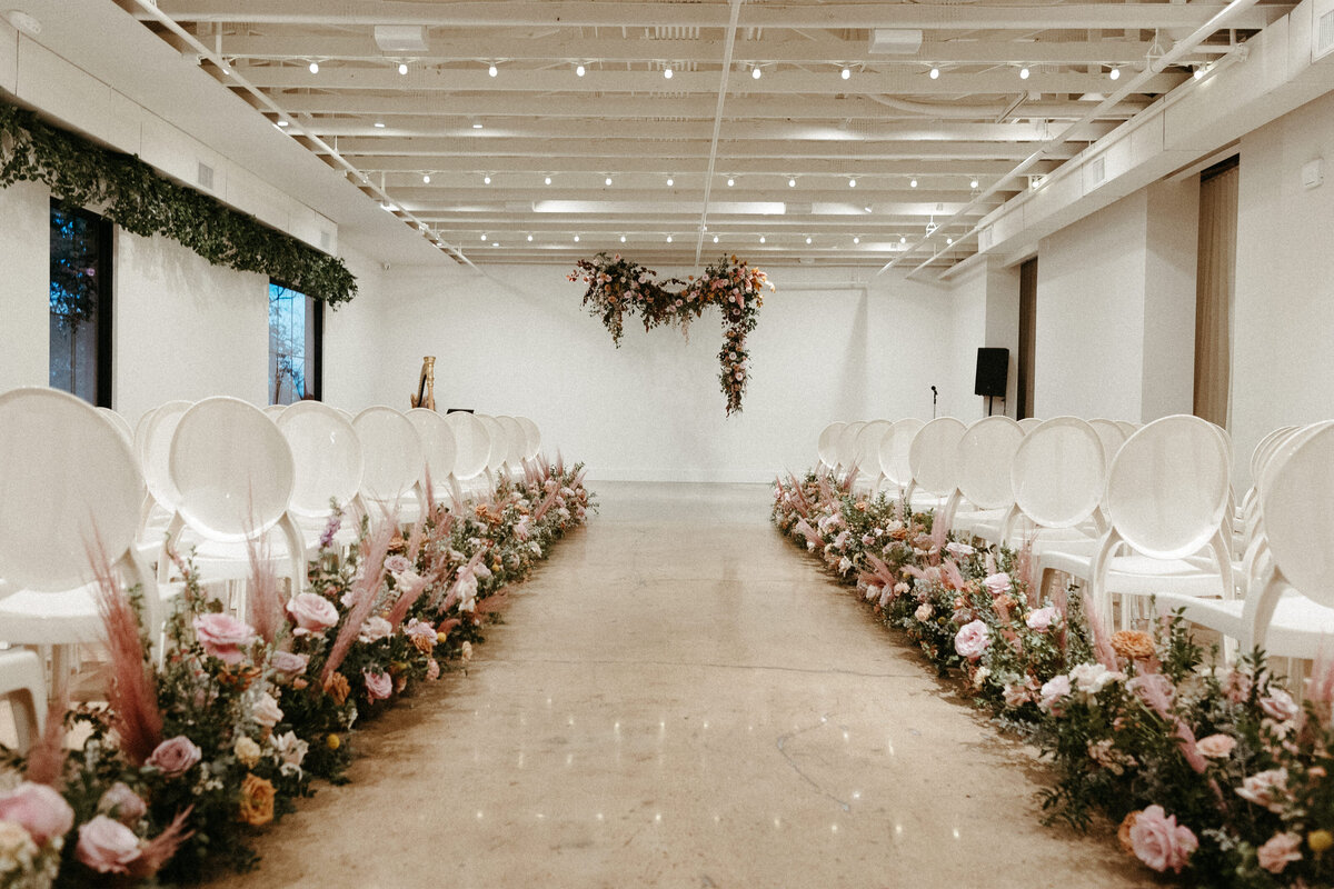 Lush aisle meadows beautifully frame the ceremony of this winter wedding with hues of dusty pink, terra cotta, cream, and sage green. Complete with petal heavy roses and pink pampas grass. Designed by Rosemary and Finch in Nashville, TN.