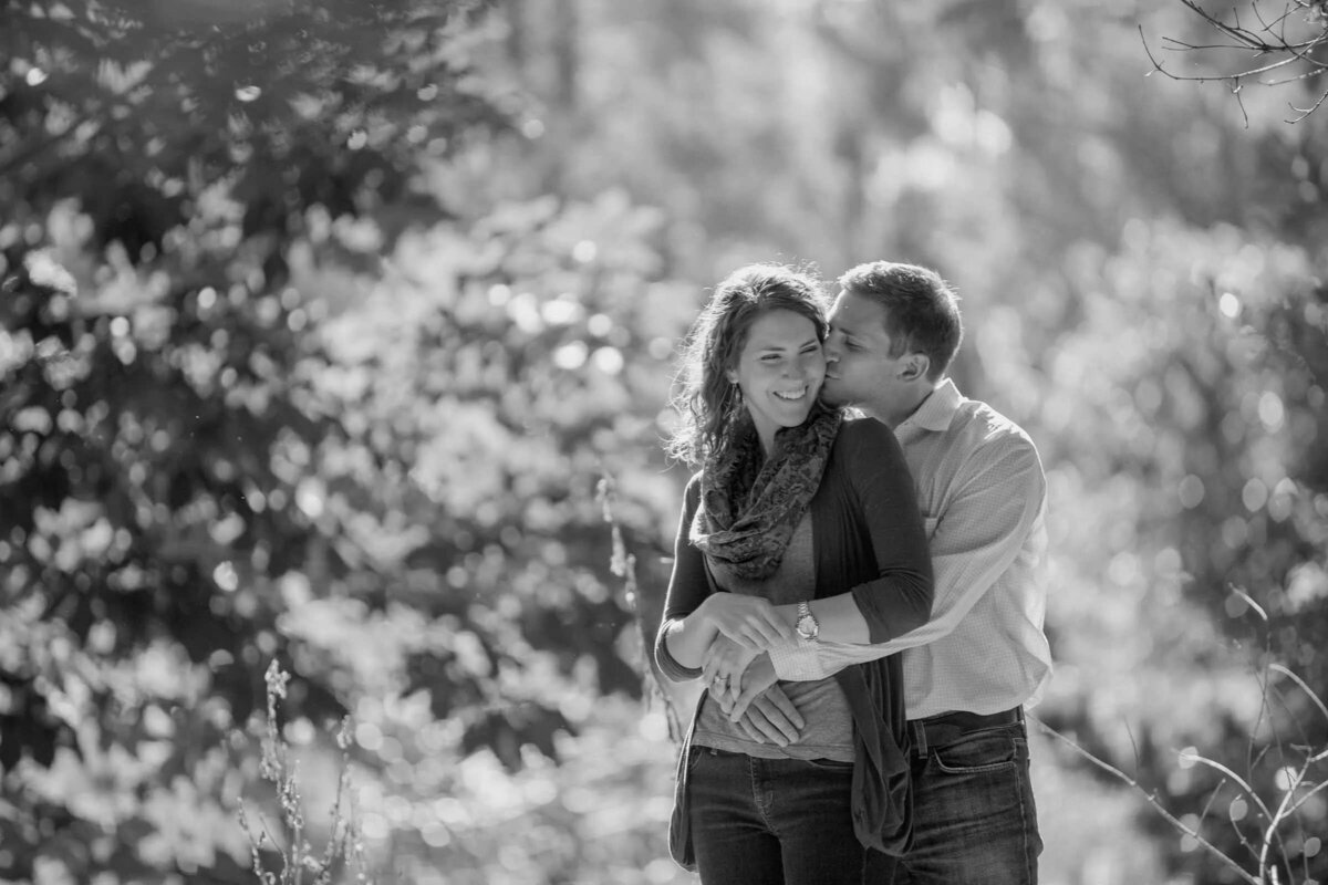 Black and white photo of a couple holding each other, with a serene and soft-focused natural background