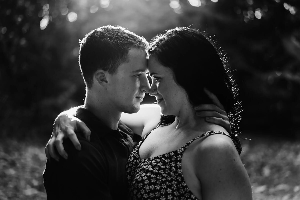 Monochrome image of a couple in a tender embrace, backlit by the soft light filtering through the trees.