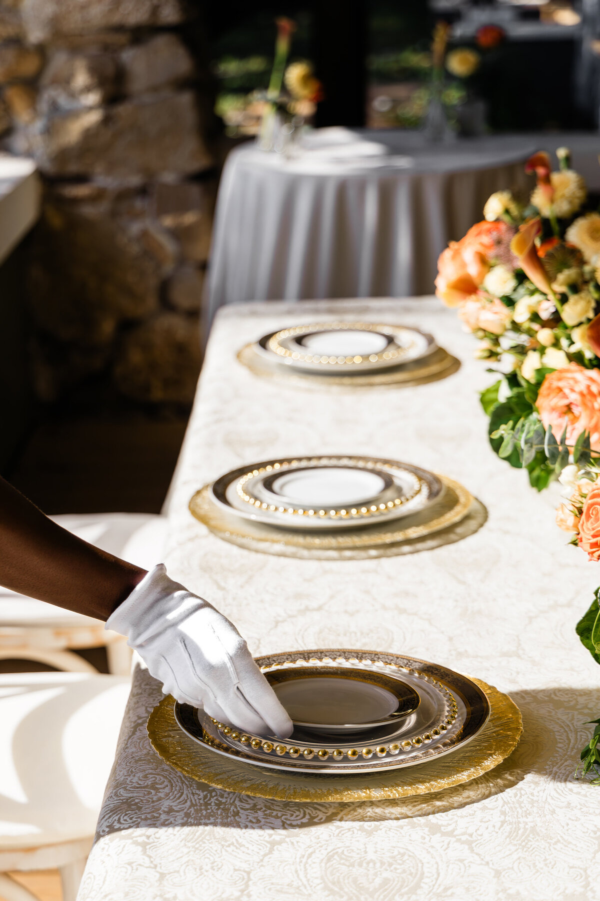 hand placing bread plate on a four plate mixed metals place setting with an orange rose and calla lily centerpiece