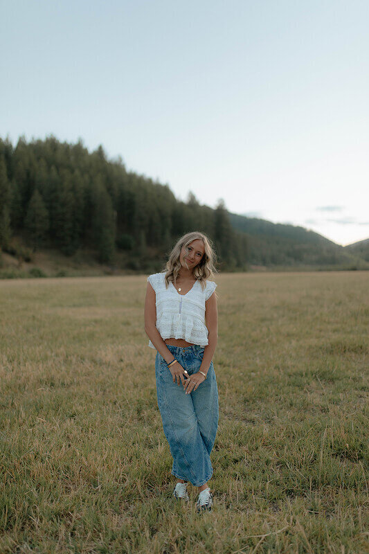 Facing the camera, a girl smiles for a portrait in near Idaho Falls, Idaho. She's touching her hands together in front of her.