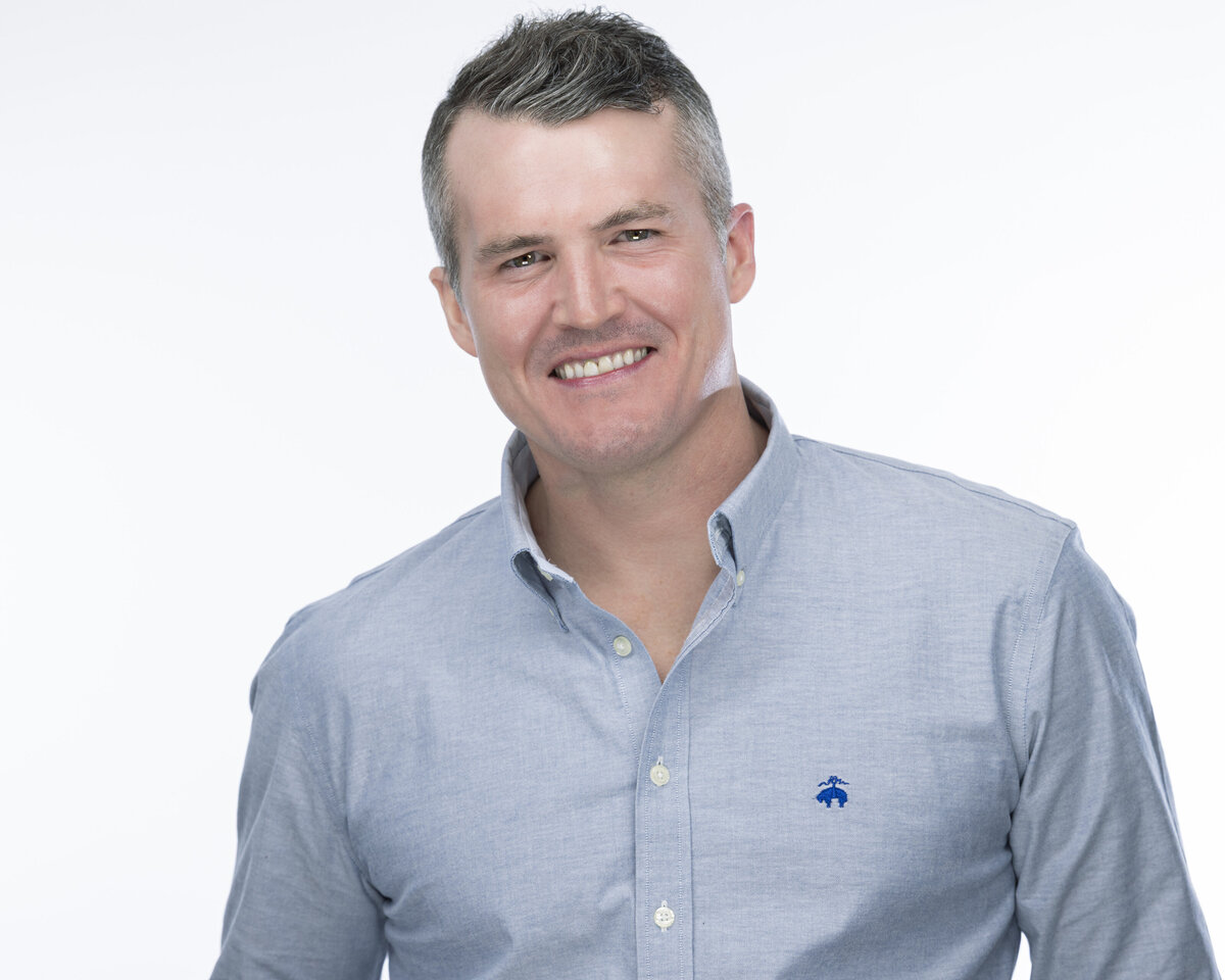 Bright studio headshot in CT of man in light blue button-down shirt, smiling against white background by Rob Faber Photography.