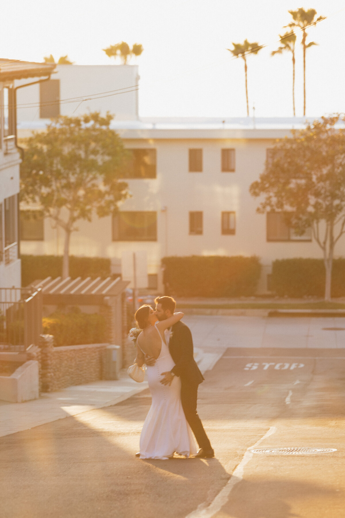 Bride and groom kissing romantically on street during golden hour, editorial wedding photographer in La Jolla.