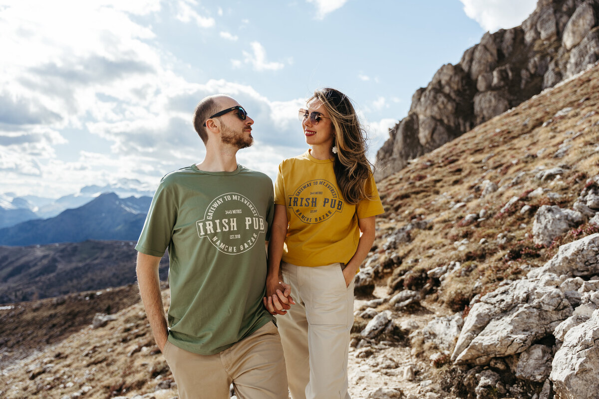 Couple holding hands on rocky path with mountains in background