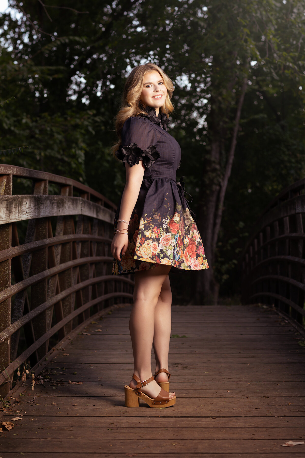 A Dallas senior photographer captures a senior girl in a floral dress standing on a bridge.