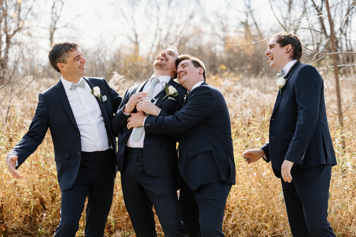 Groom and his groomsmen hugging and laughing while congratulating the groom
