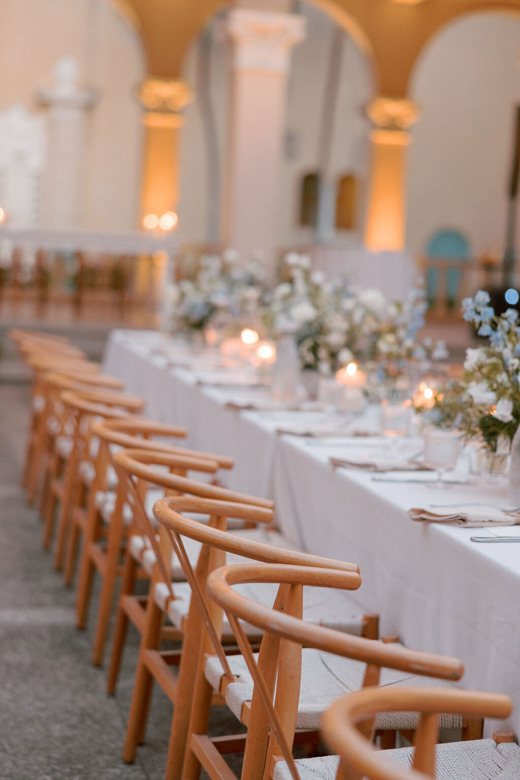 wedding reception with arches in the distant and long wedding table with wishbone chairs