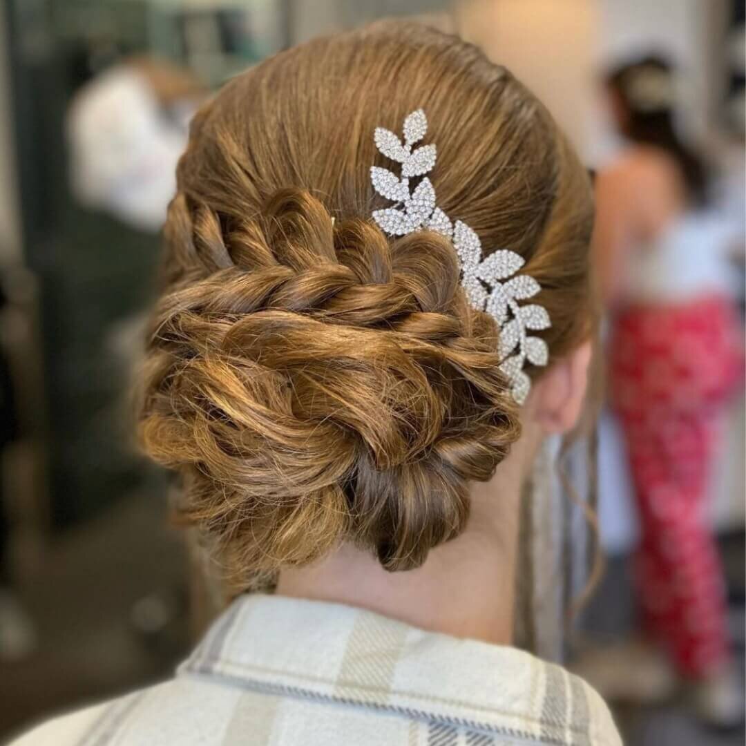 A woman with an elegant braided updo adorned with a decorative hairpiece, showcasing a bridal hairstyle created by 212 Salon, Spa, & Barbershop.