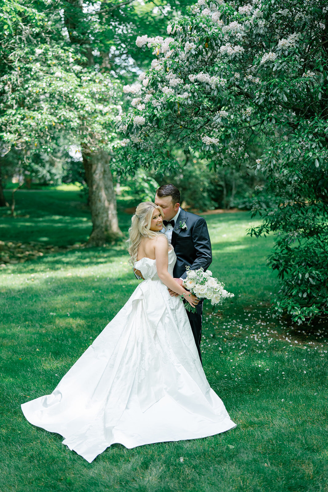 Bride and groom embracing under blossoming garden trees during romantic wedding portraits at Old Edwards Inn in Highlands, North Carolina.
