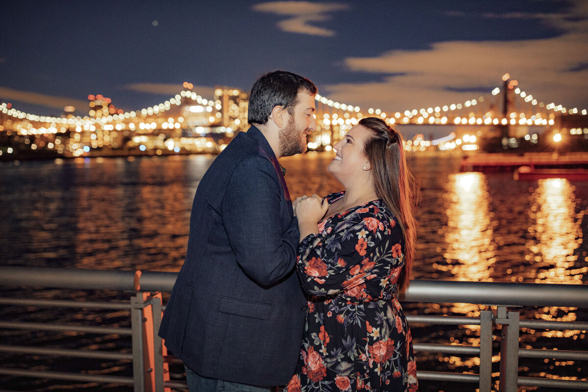 Couple holding hands during nighttime engagement photo on Brooklyn Bridge in New York City