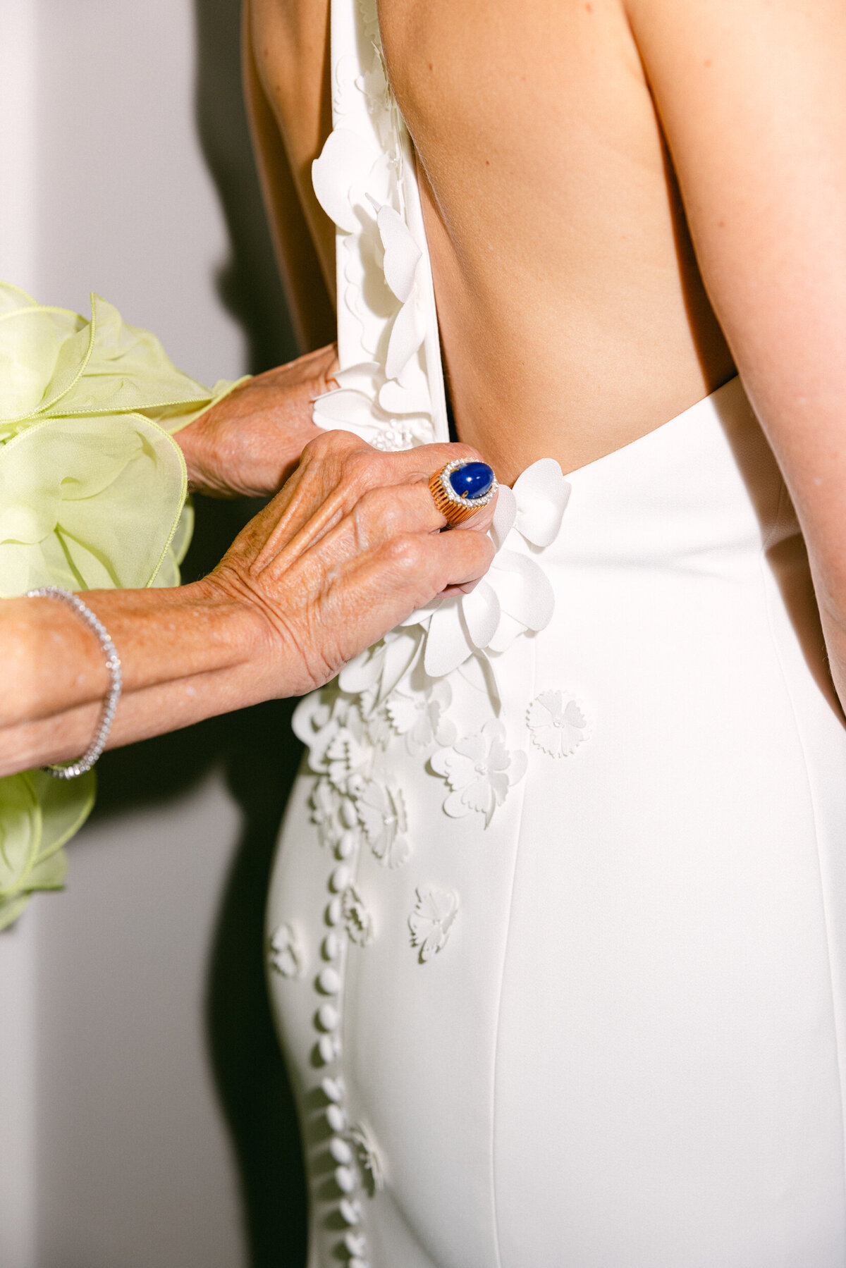 A wedding day photo of the brides mom zipping up her daughters white wedding dress