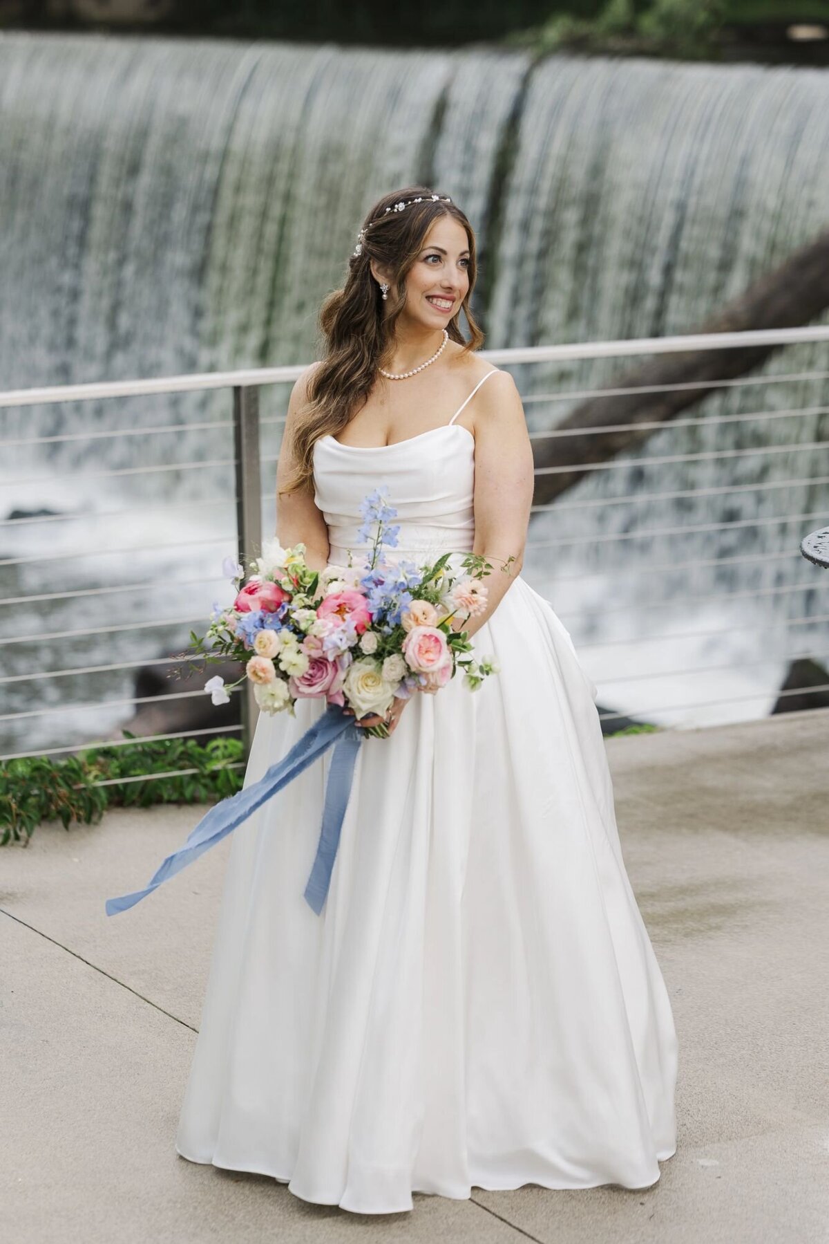 Bride stands with bouquet in front of Beacon Falls at her Roundhouse wedding