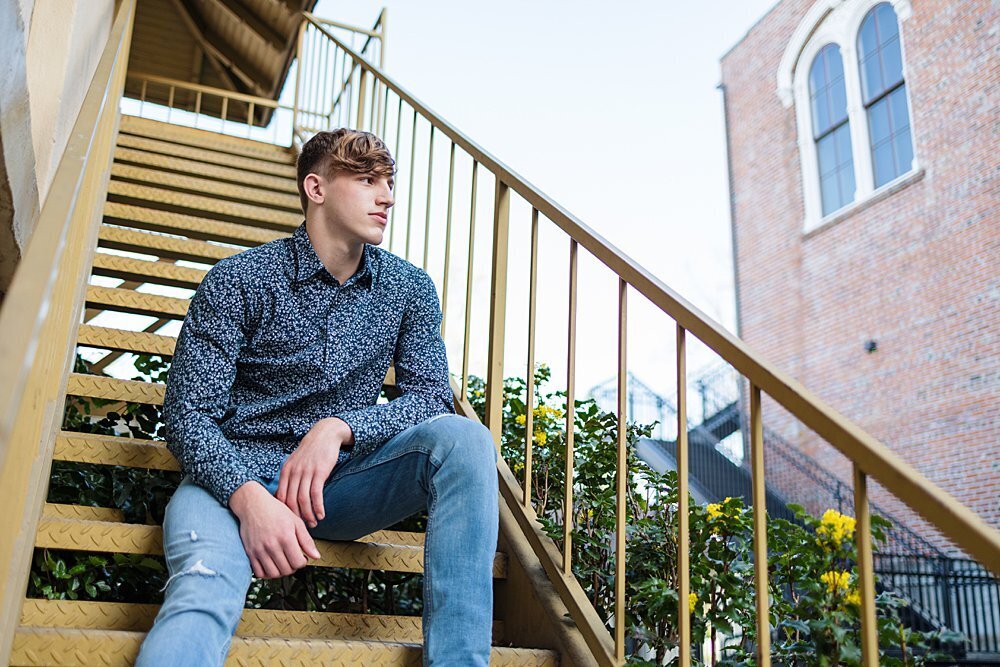 senior guy sitting on yellow stairs with brick building behind him