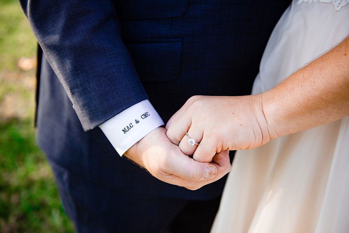 The groom shows off his embroidered sleeve cuff as he holds hands with the bride who is wearing a diamond solitaire engagement ring and thin gold bracelet