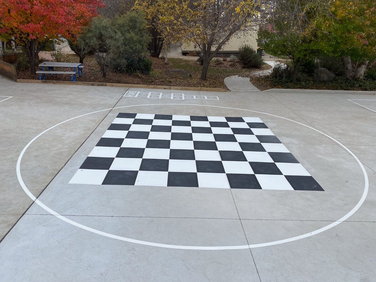 Line marking in a primary school play area of black and white checkers on a concrete floor.