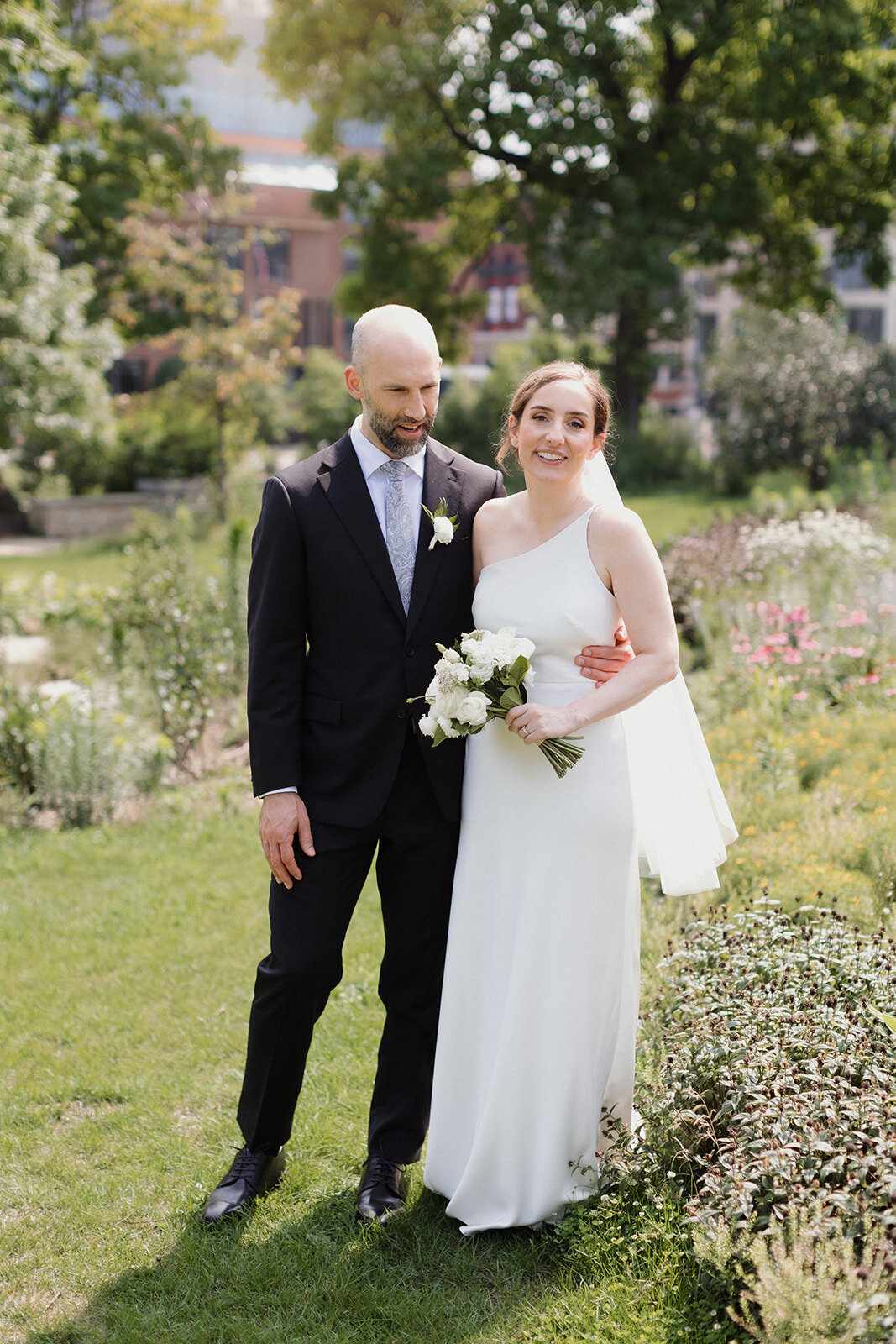 couple pauses in Chicago History Museum garden in the summer as the flowers bloom. Bride looks at camera.