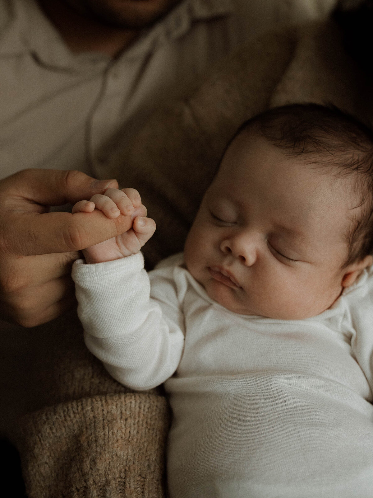 Baby holding dad's finger during in-home newborn session in Chino Hills.