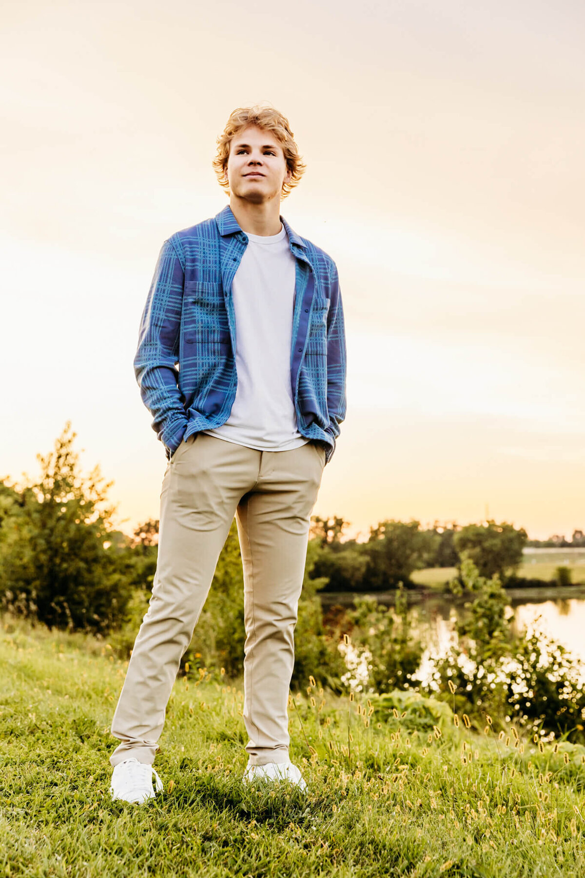 high school boy standing with his hands in his pockets and looking out into the distance at sunset.