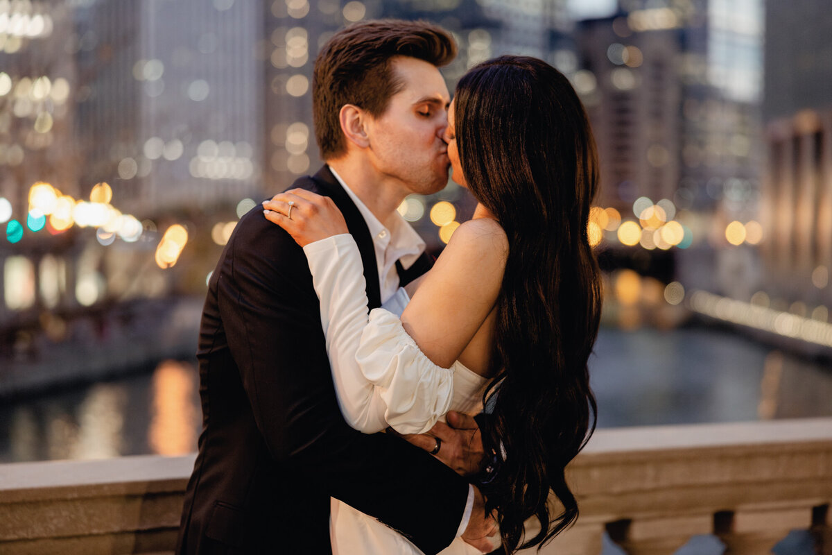 A couple embraces at dusk along Michigan Avenue and the Chicago River, with the city lights creating a romantic and timeless backdrop.