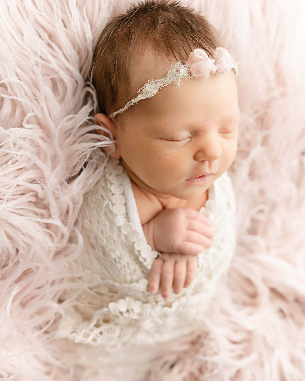 baby photo of girl on pink fuzzy backdrop wearing a pink bow. Captured in Portland Oregon photographystudio.