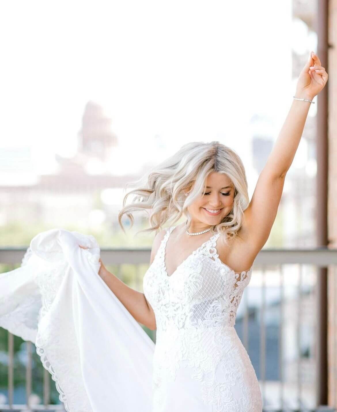 Bride with soft blonde curls and lace wedding dress twirling on her big day | Austin wedding hair stylist near me