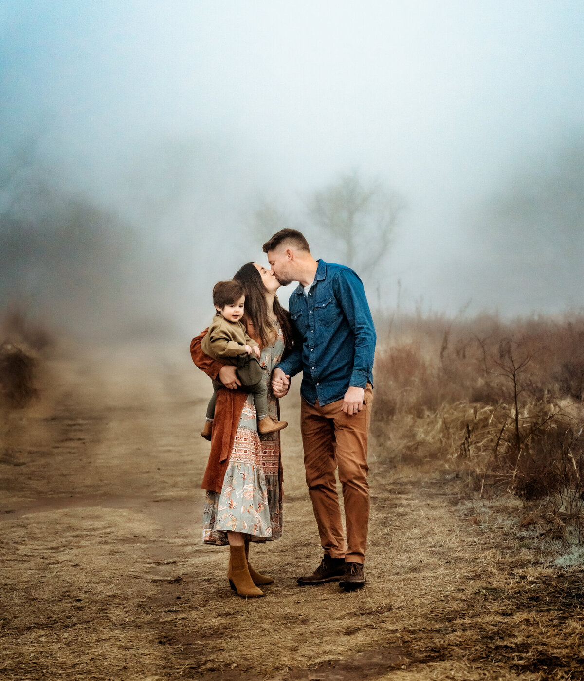 Family Photographer, a man and woman kiss on a country road, she holds their young son