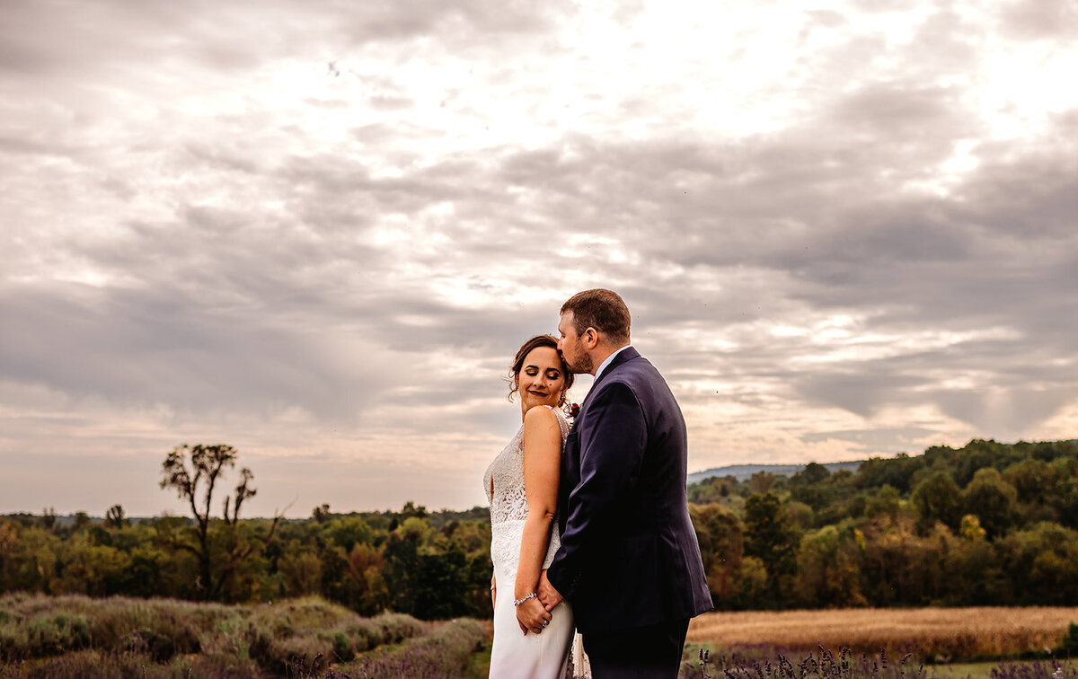 Maryland wedding photographer captures outdoor bridal portraits with groom standing behind his bride and holding her hands while he kisses the top of her head