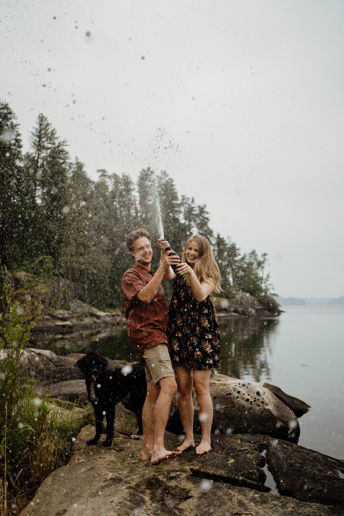 couple popping champagne by lake