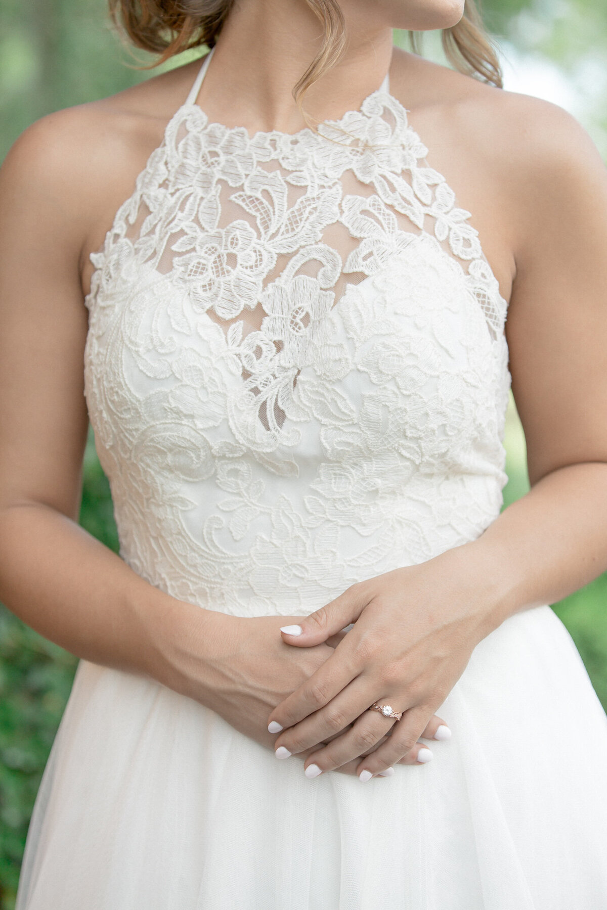 A close up of the brides hands  showcasing her engagement ring and the lace on her bodice just before her wedding