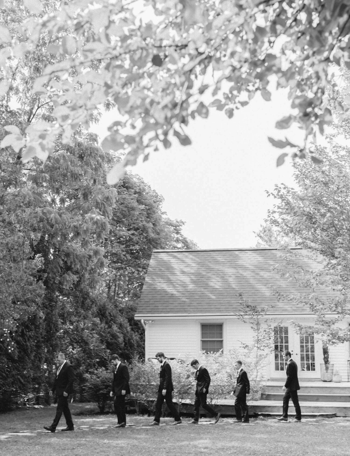 line of groomsmen walk to ceremony at Glass House Community wedding, Michigan