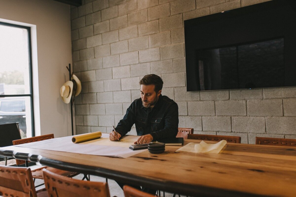 man sitting at a long table drawing up design plans