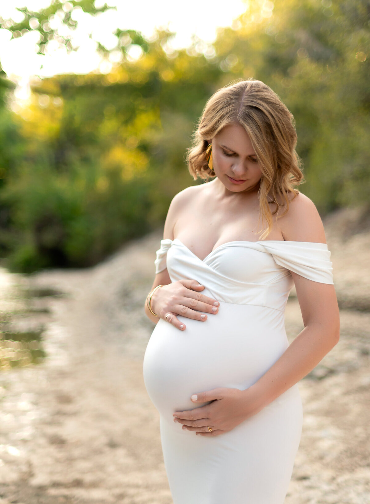 Maternity portrait of woman in a white off-the-shoulder gown by the water in Leander, Texas