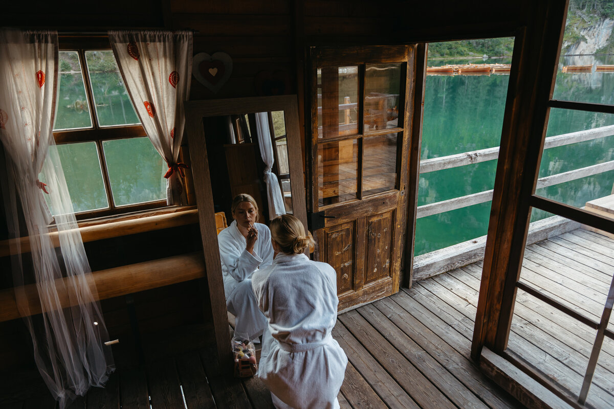 Bride in robe on wooden balcony at Lago di Braies boathouse