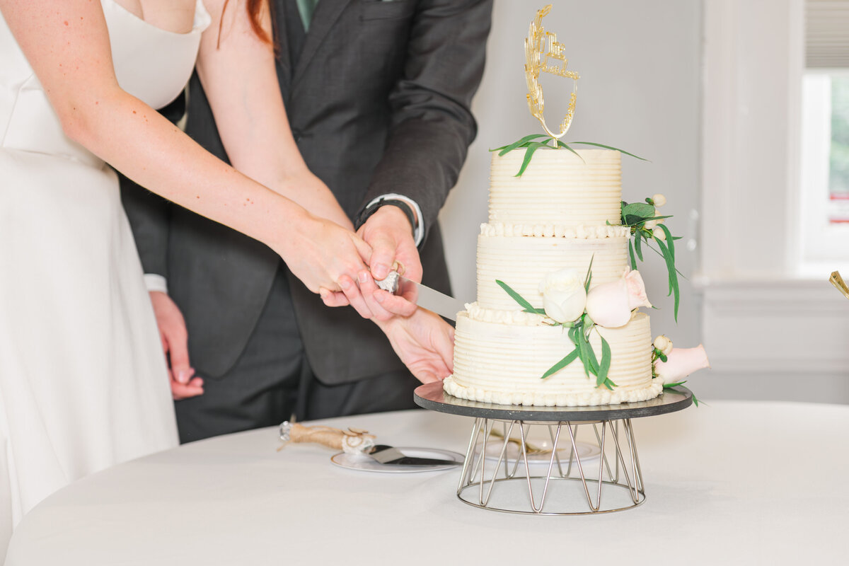 cake cutting of a three tier cake with flowers and greenery, complete with a gold topper