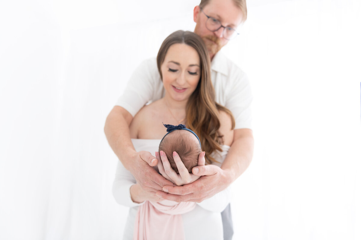 Happy new parents hold their newborn baby in their hands out in front of them