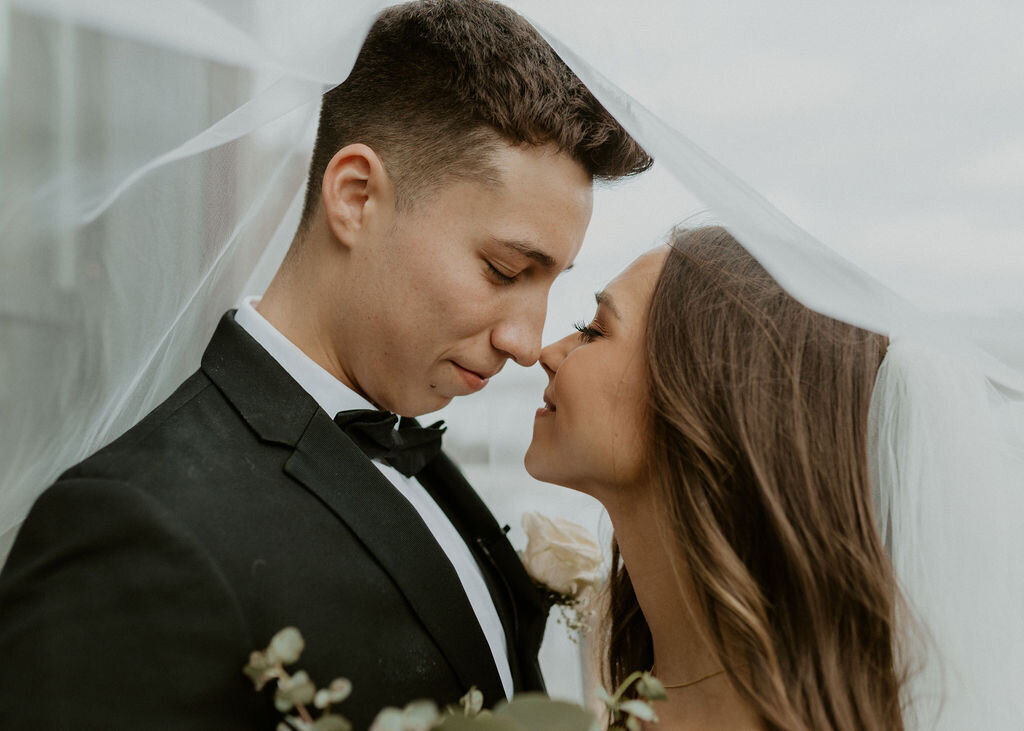 Bride and groom smiling and touching noses under a white wedding veil