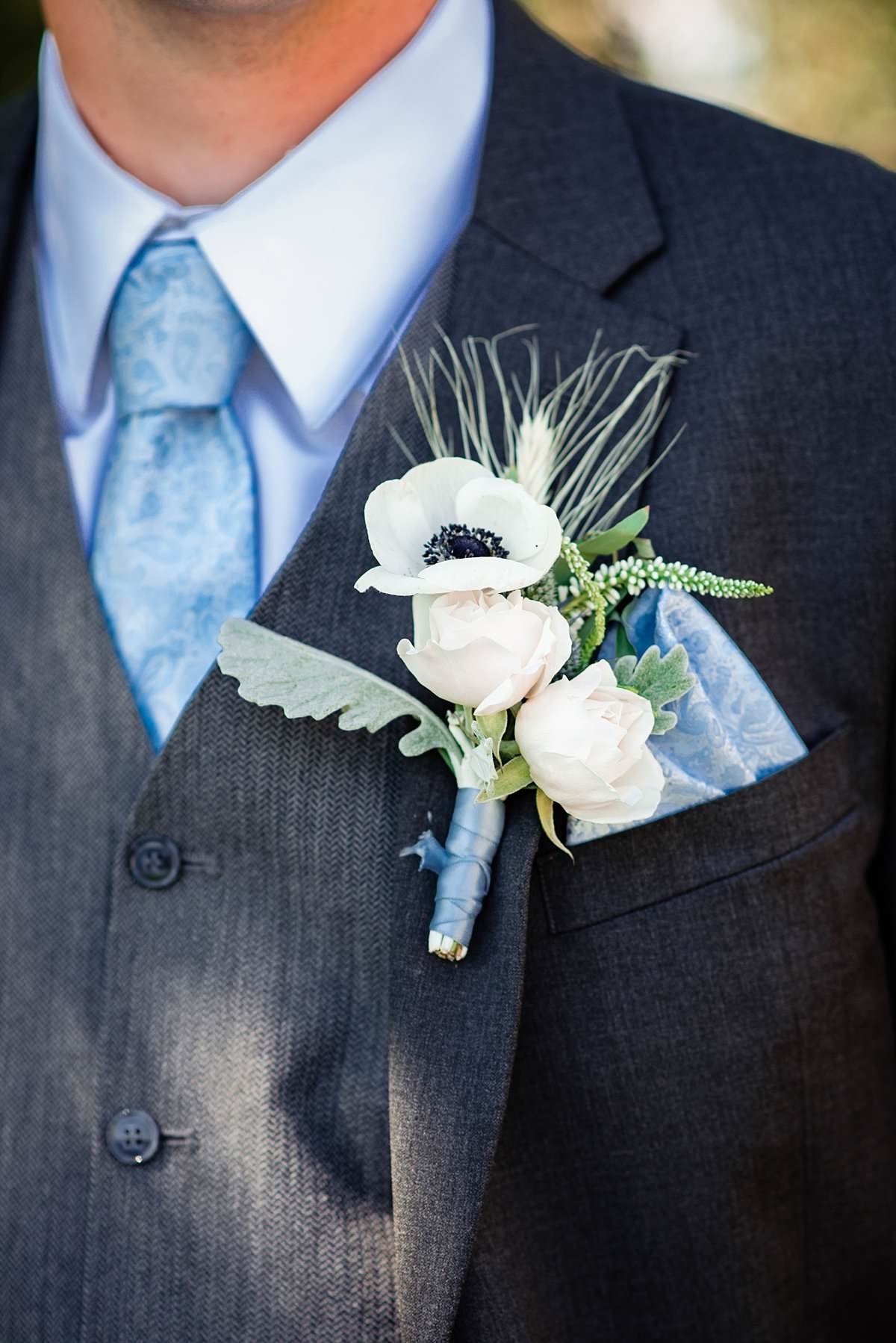 Close up photo of grooms boutonniere with anemone, roses and wheat