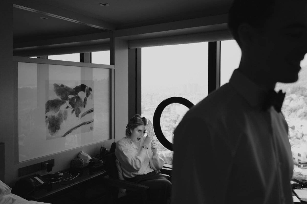 the groom fixing his suit while the bride is retouching her makeup at the background