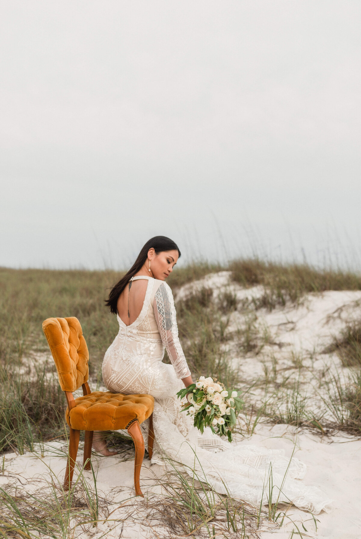 portrait of asian bride in bridal dress and veil on orange velvet chair  beach path - taken by panama city fl photographer Brittney Stanley