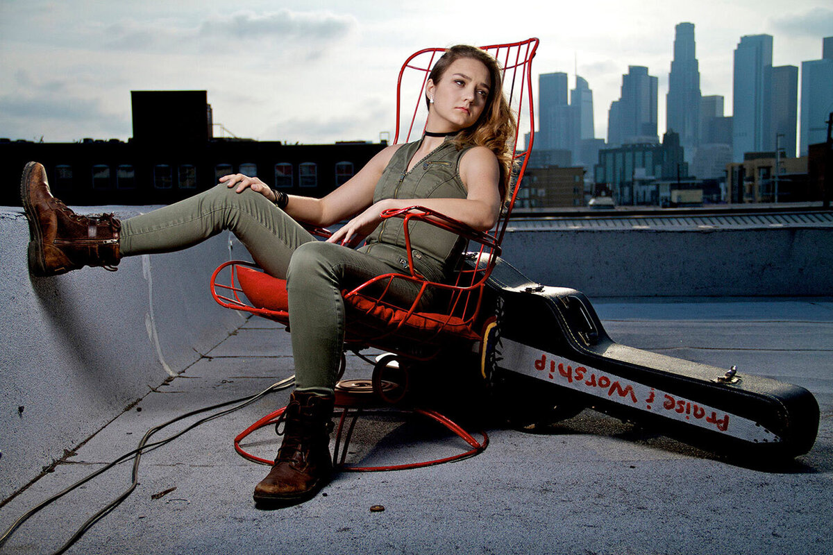 Female Musician portrait Stefani Jai sitting on Los Angeles rooftop in red metal chair guitar case on ground behind her Just Play Something Gallery