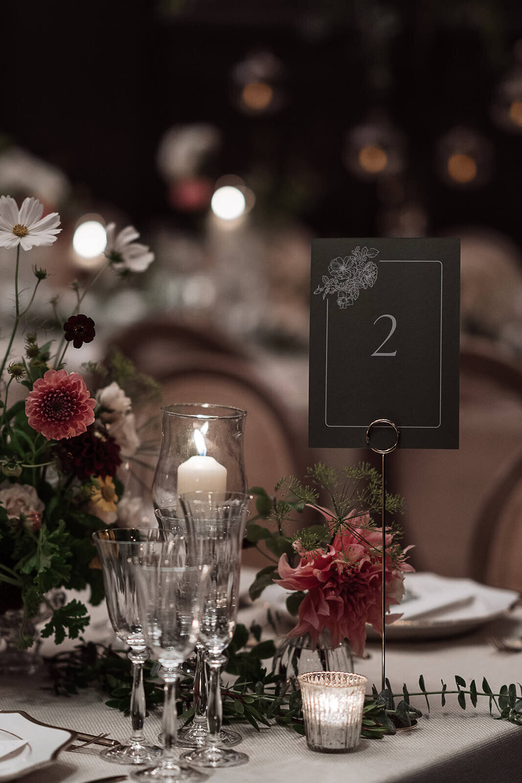 closeup of a candlelit intimate wedding dinner table showing a custom table number and floral arrangements with cosmos and honeycomb dahlia