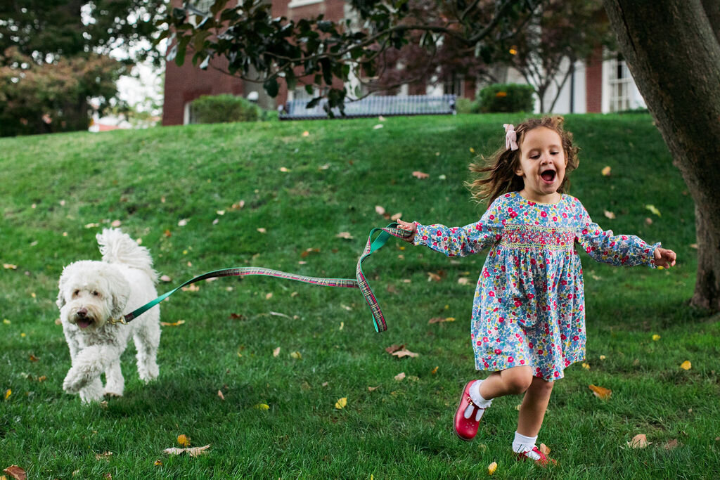 A young girl runs with a white fluffy dog.