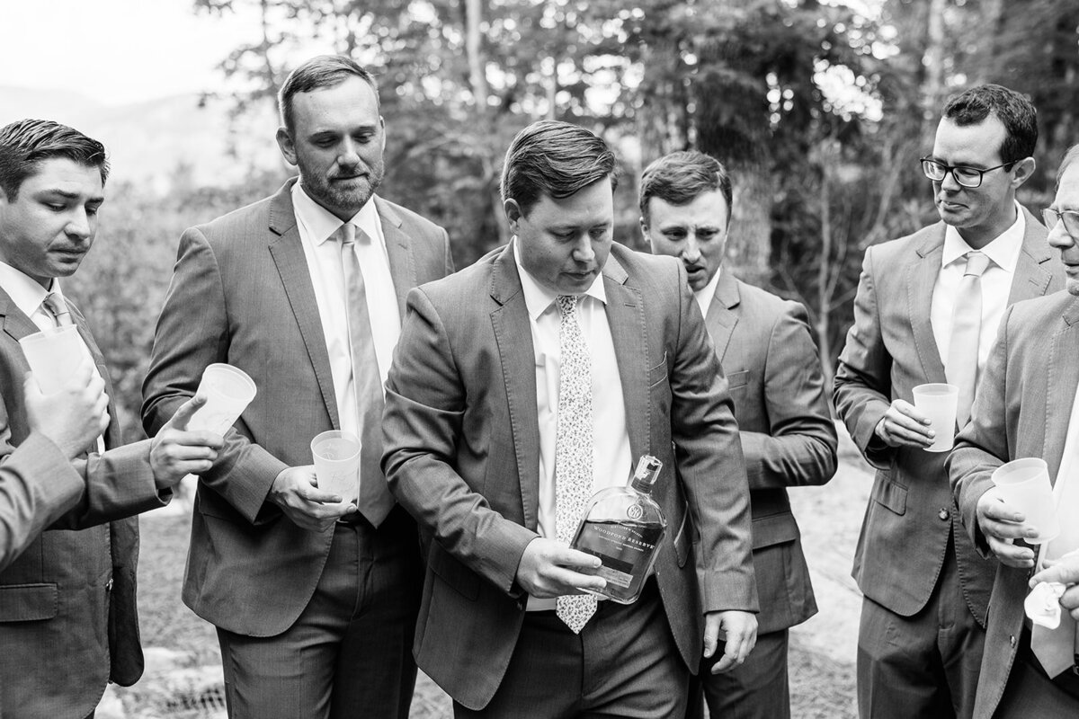 Black and White photo of a groom and his groomsmen passing out bourbon to each other. 